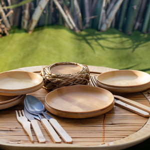 Some bamboo plates and cutlery in a outdoor table scene